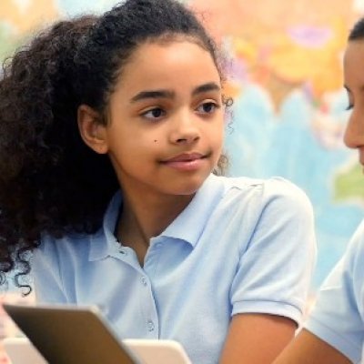 School girls sit at desk looking at iPad.